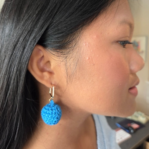 Close-up of a person wearing blue crochet ball earrings.